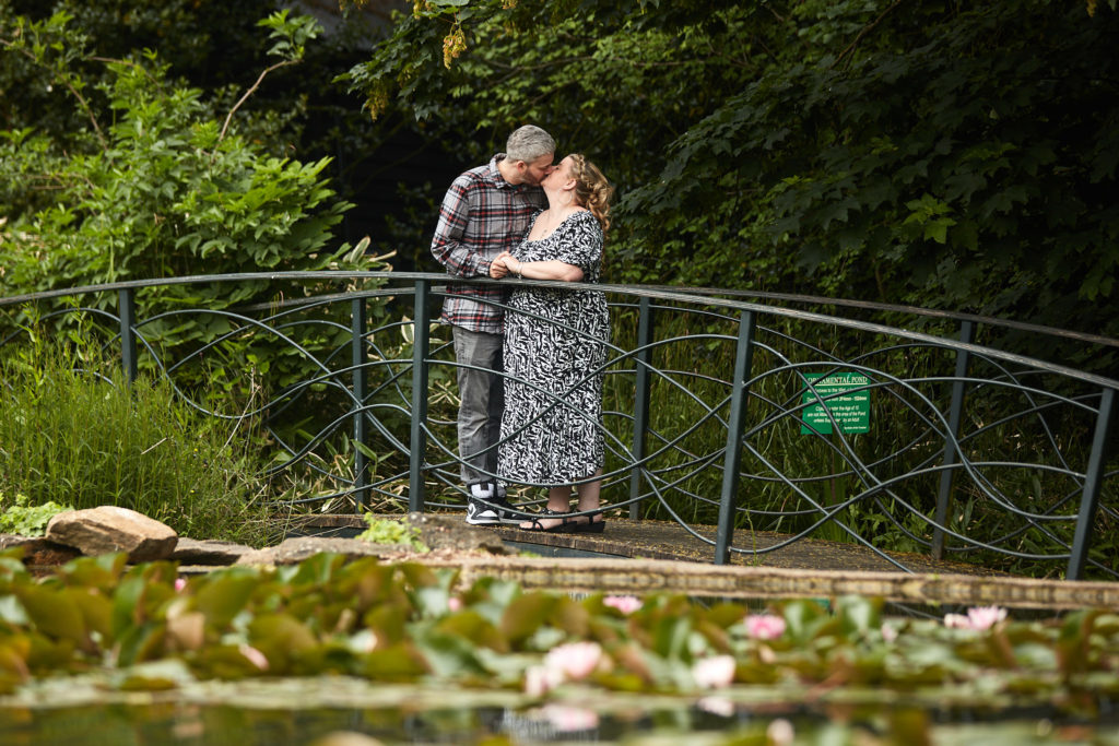 Engaged couple standing on a footbridge over a lily pond