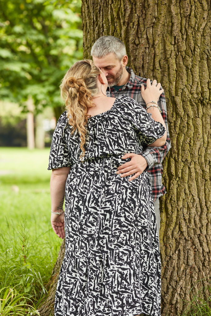 Engaged couple embracing against a tree trunk on their park engagement shoot in Braintree, Essex