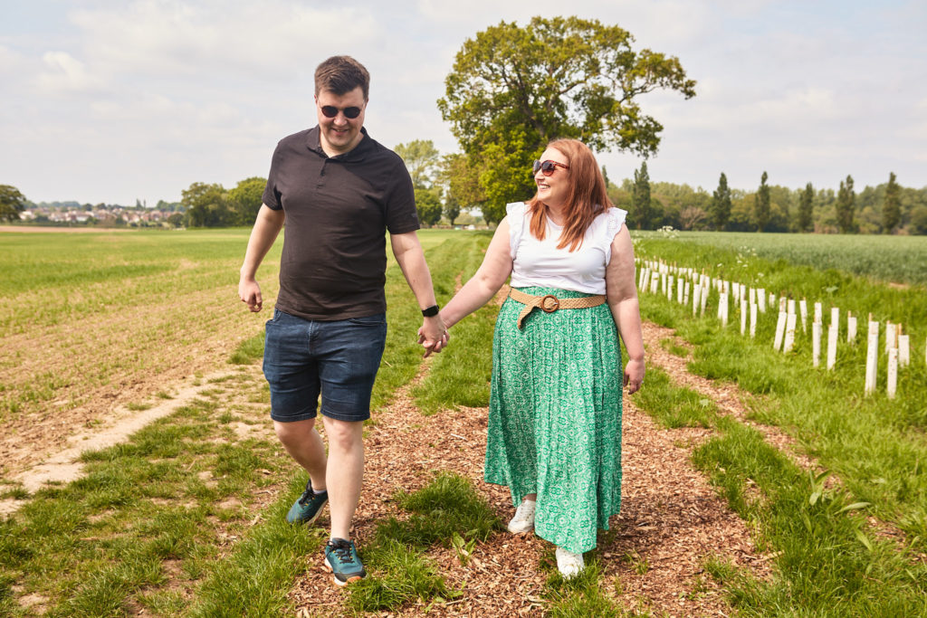 Engaged couple walking hand in hand along a field path near Clacton