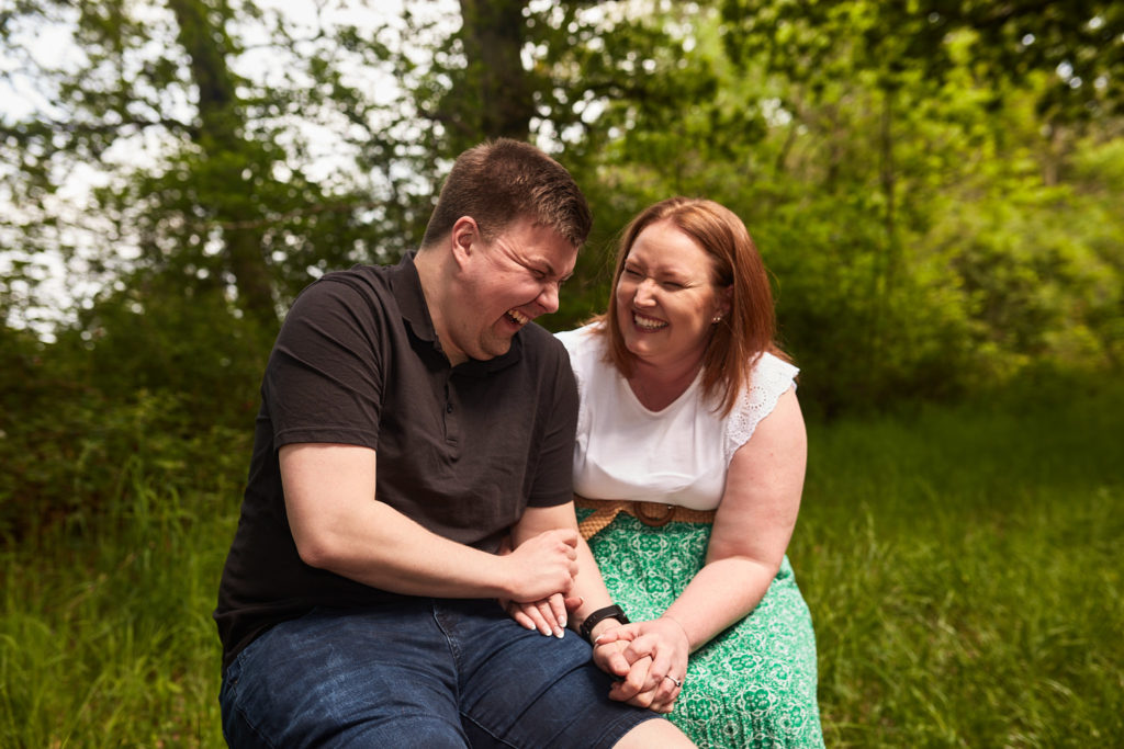 Engaged couple laughing together as they sit in the woods