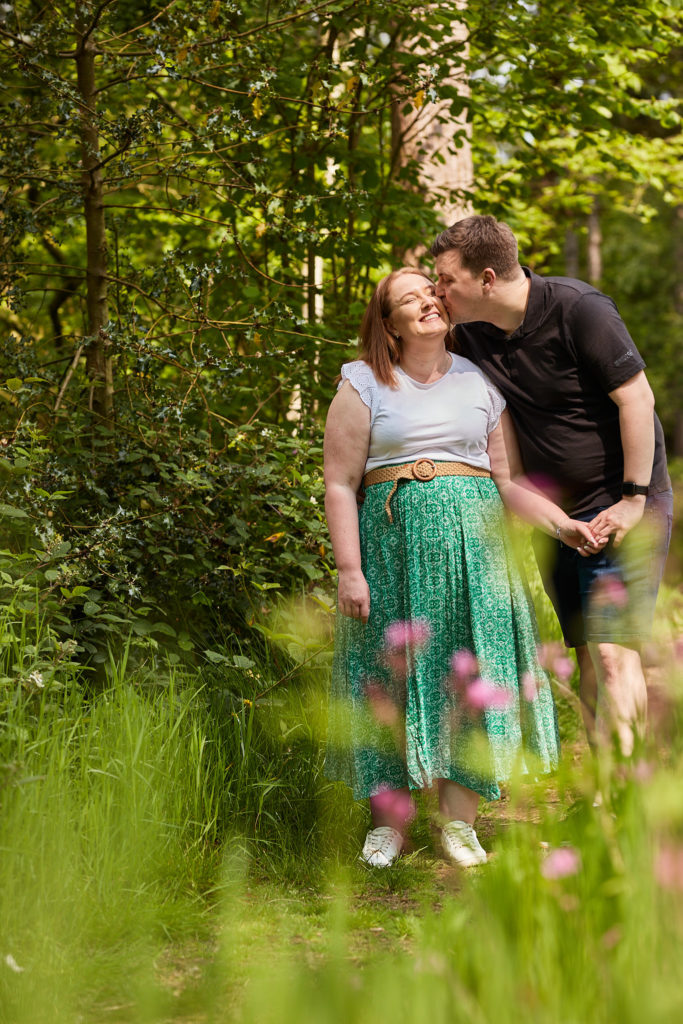 Man hugging his laughing fiancée from behind among wild flowers