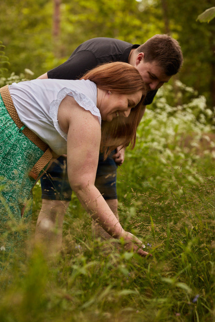 Engaged couple bending down to look at wild flowers together