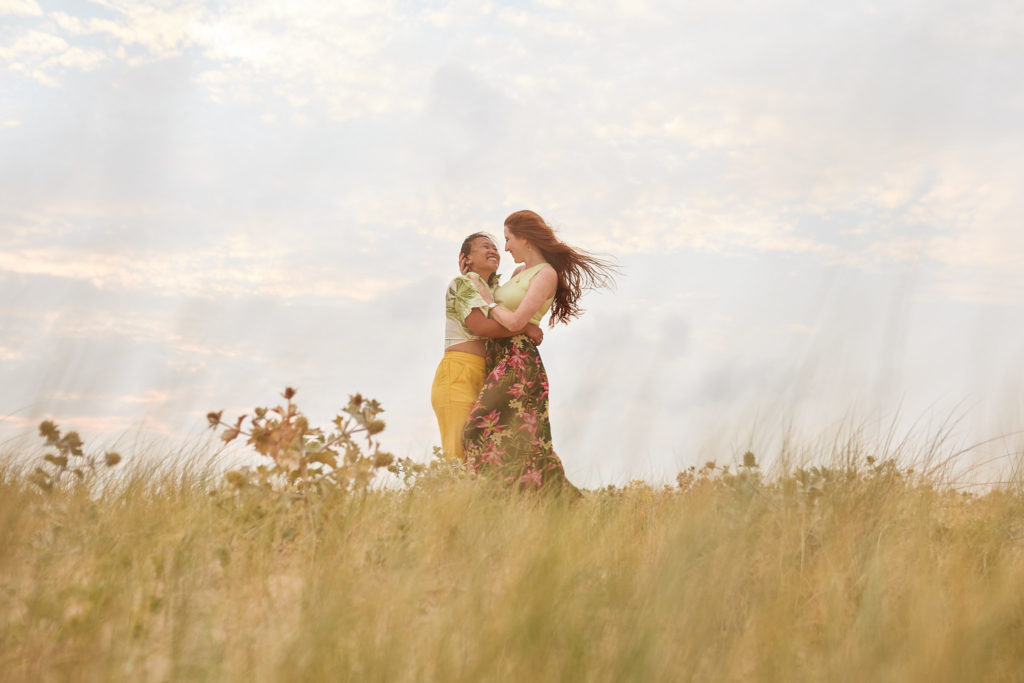 Engaged couple hugging in the dune grass on a windy beach