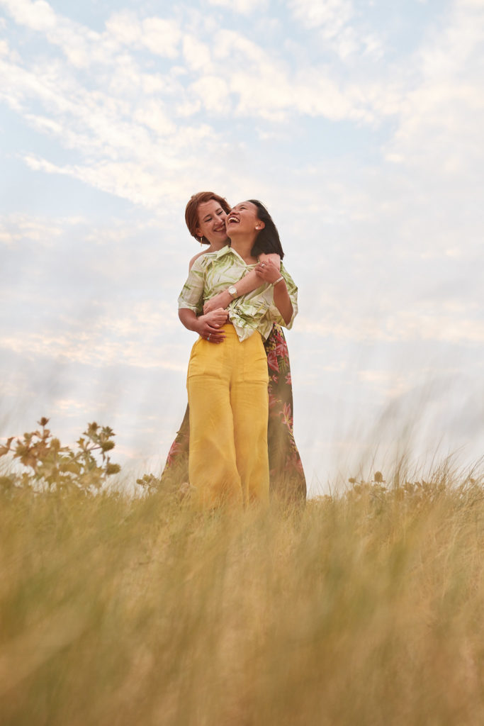 Engaged couple hugging in the dunes with their hair blowing in the wind