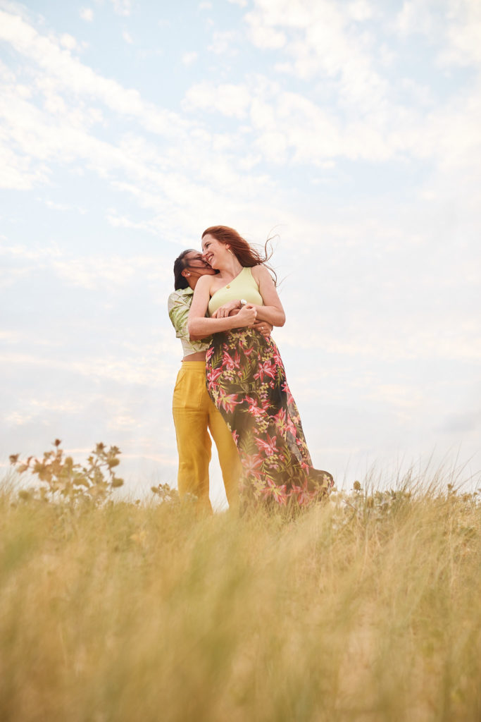 Two women embracing in the long dune grass on their same-sex engagement shoot