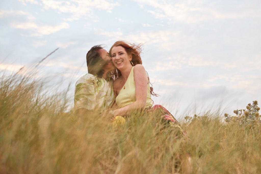 Engaged couple cuddling in the dune grass