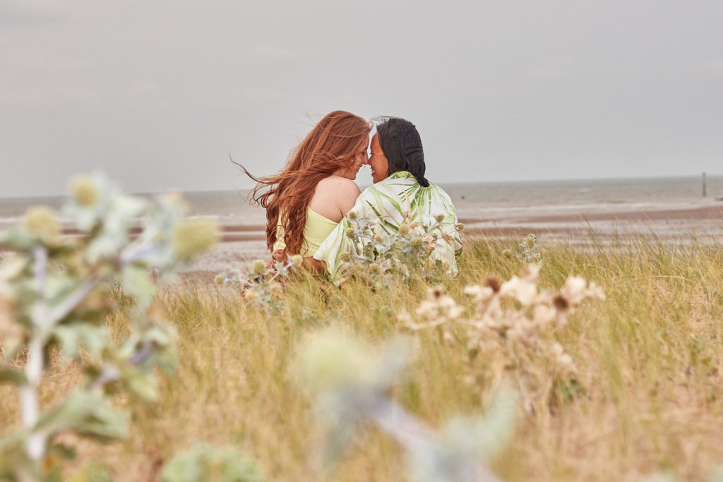 Engaged couple looking out to sea from the dunes