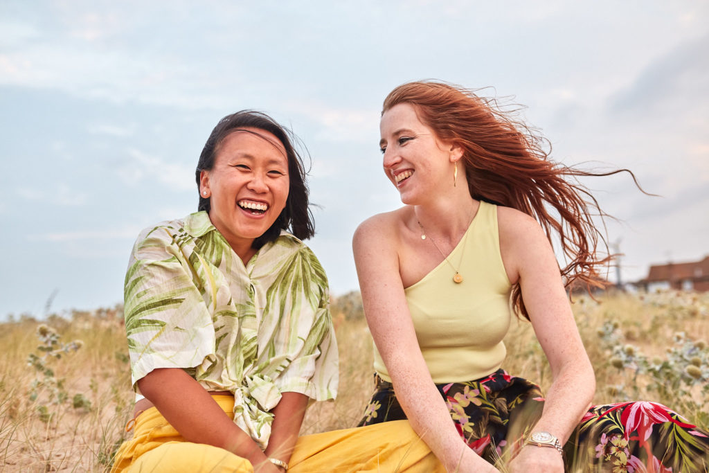 Two women laughing as they sit together in the dunes