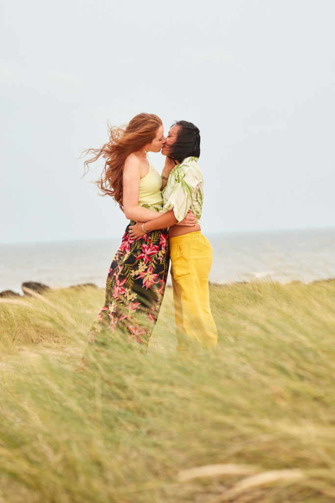Two women kissing in the dune grass on their LGBTQ engagement shoot in Clacton, Essex