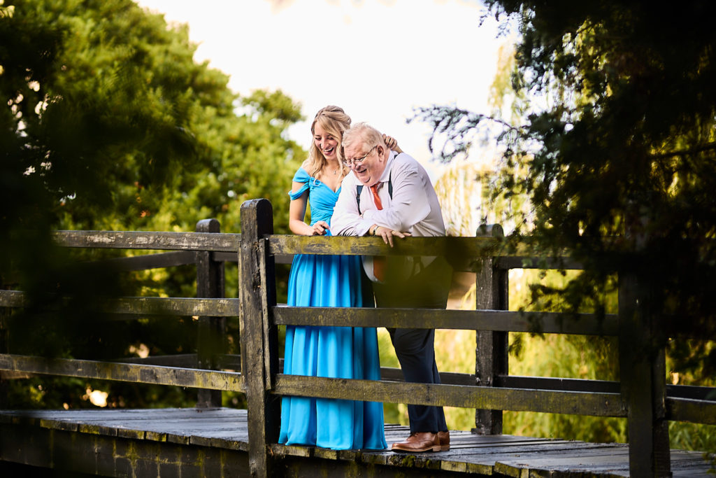 Bridesmaid in a blue dress hugging a guest on a wooden footbridge