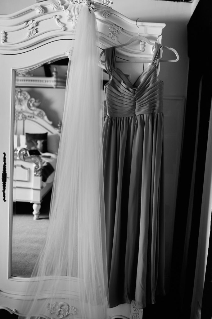 Black and white photo of a veil and a pleated dress hanging on an ornate wardrobe