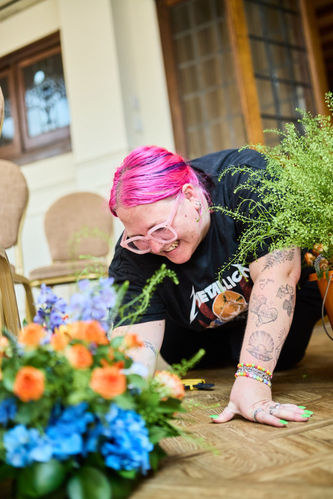 Florist with pink hair laughing as she arranges blue and orange wedding flowers