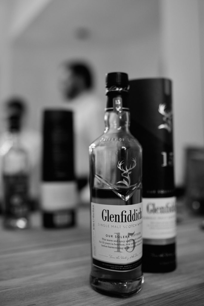 Black and white photo of a bottle of Glenfiddich whisky with the groomsmen blurred behind