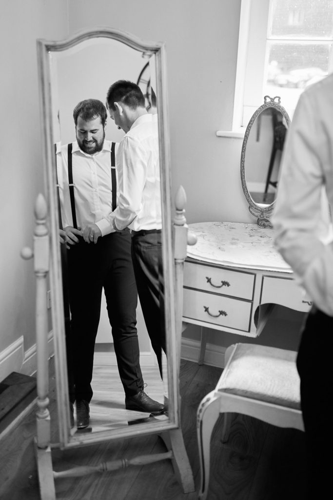Black and white photo of the groom in braces reflected in a full-length mirror