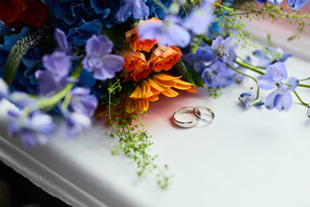Wedding rings on a windowsill beside blue and orange flowers