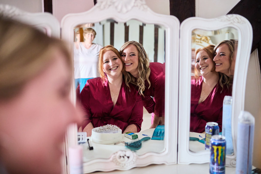Bride and bridesmaid smiling in the dressing table mirror during bridal prep