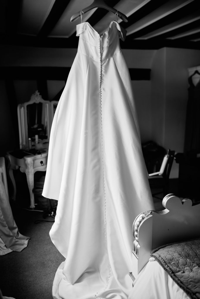 Black and white photo of the wedding dress hanging from a beam at Prested Hall