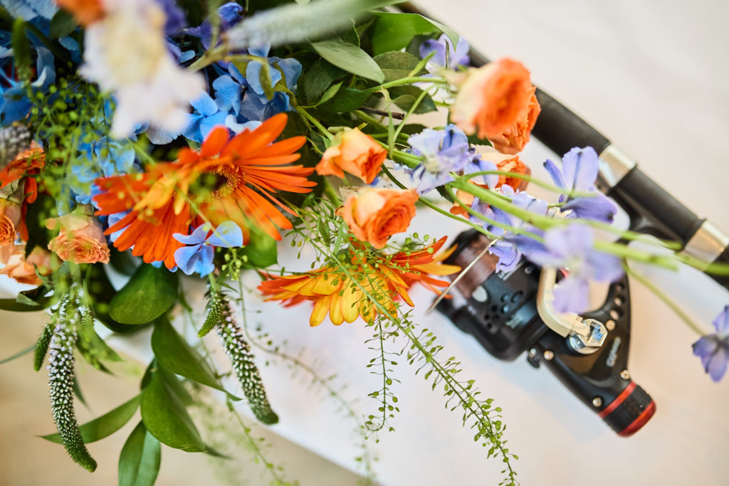 Fishing rod and reel resting beside orange and blue wedding flowers