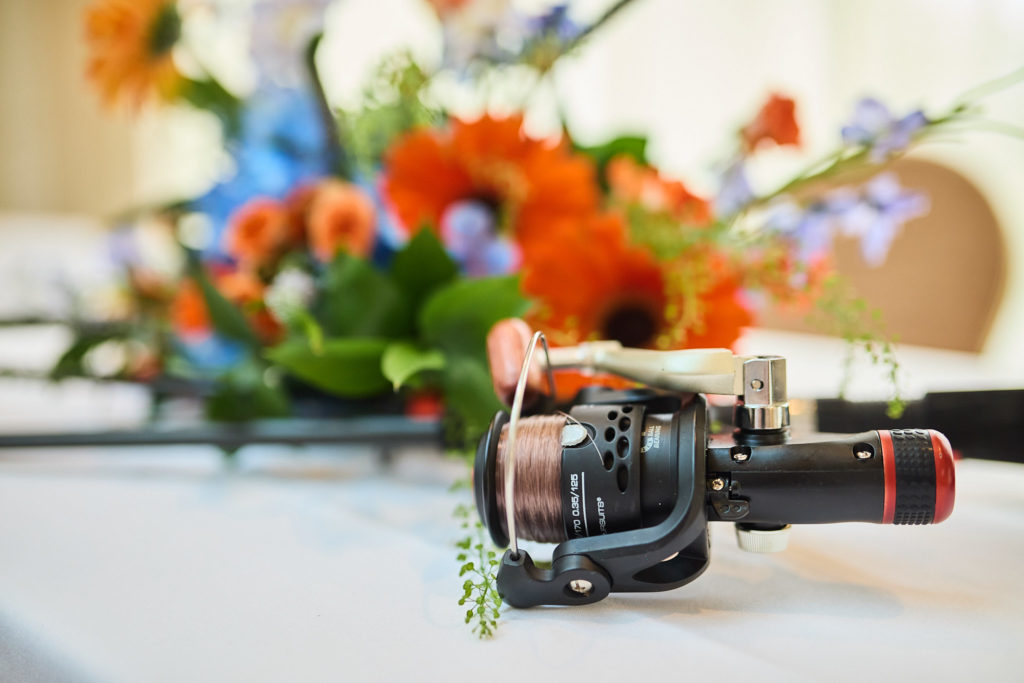 Close-up of a fishing reel beside orange and blue wedding flowers