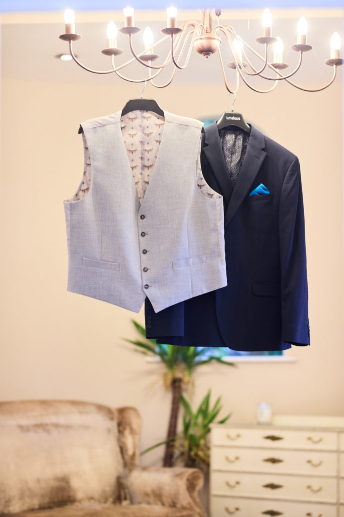 Grey waistcoat and navy suit jacket hanging from a chandelier