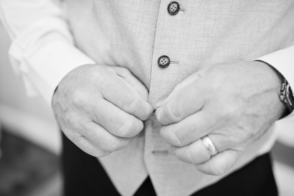 Black and white close-up of hands buttoning a waistcoat