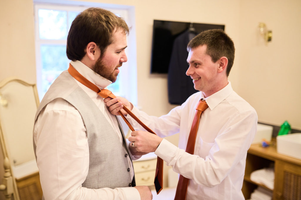 Groomsman tying the groom's orange tie
