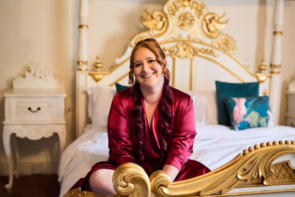 Bride in a burgundy robe laughing on an ornate gold bed