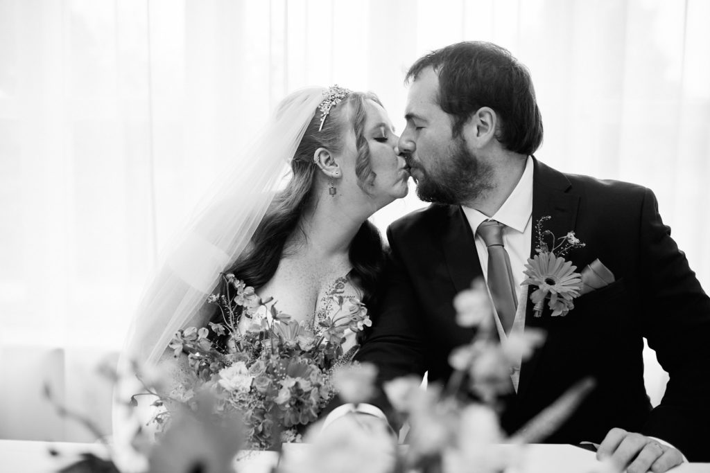Black and white photo of the bride and groom kissing behind a table of flowers