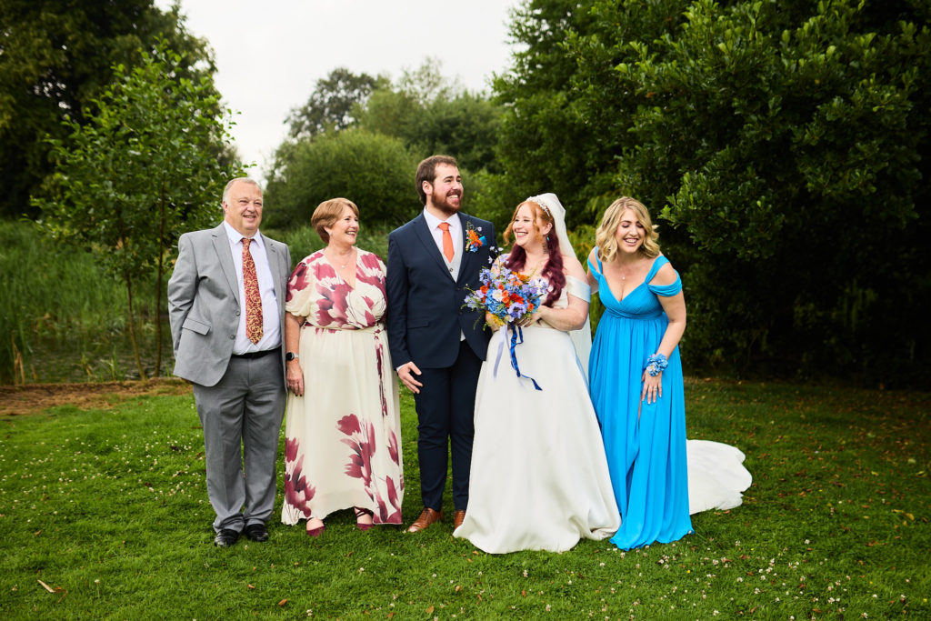 Bride and groom with family and a bridesmaid in blue on the lawn
