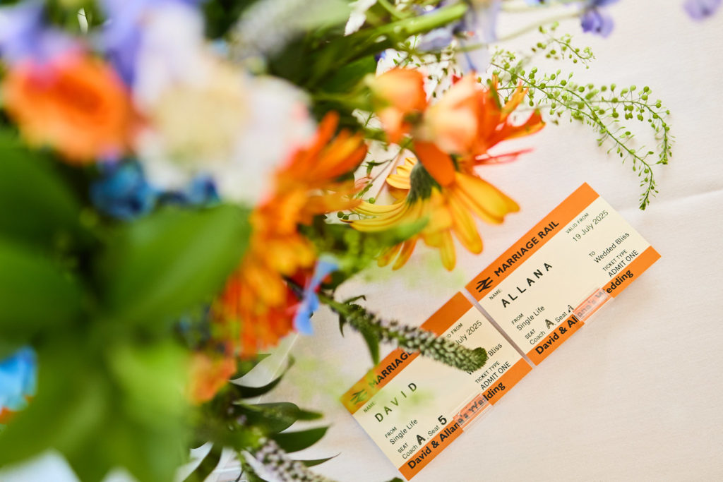 Vintage-style train tickets used as place cards beside blue and orange wedding flowers