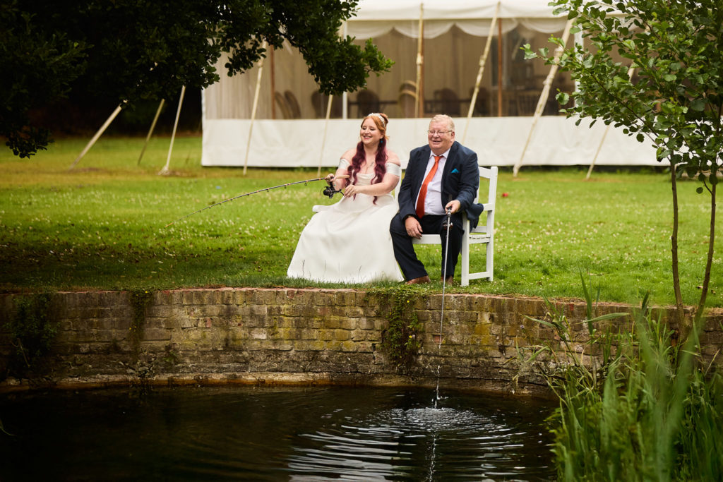 Bride and groom sitting on a white bench beside the pond and fountain at Prested Hall