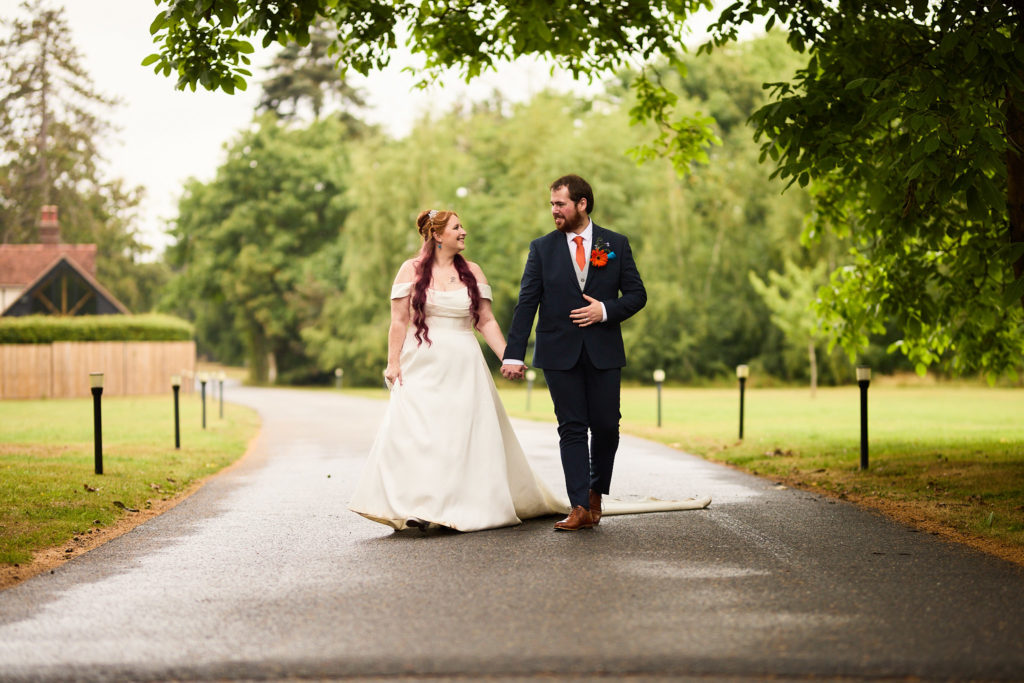 Bride and groom walking hand in hand along the tree-lined drive at Prested Hall