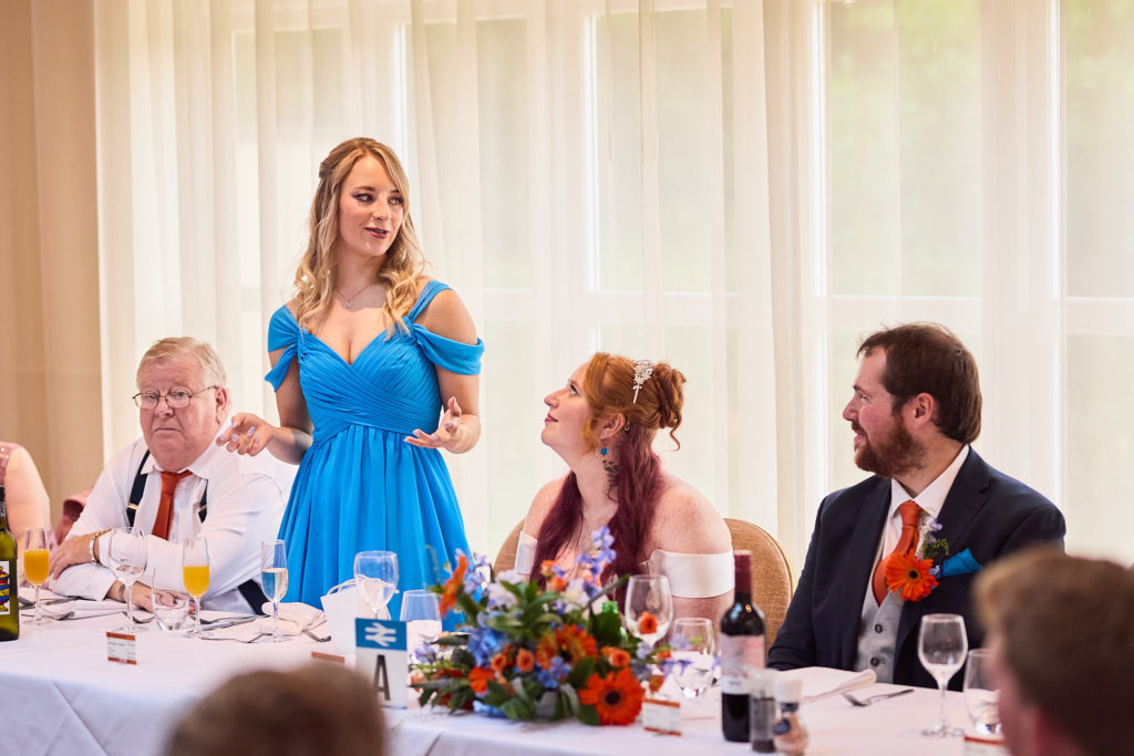Bridesmaid in a blue dress giving a speech at the top table