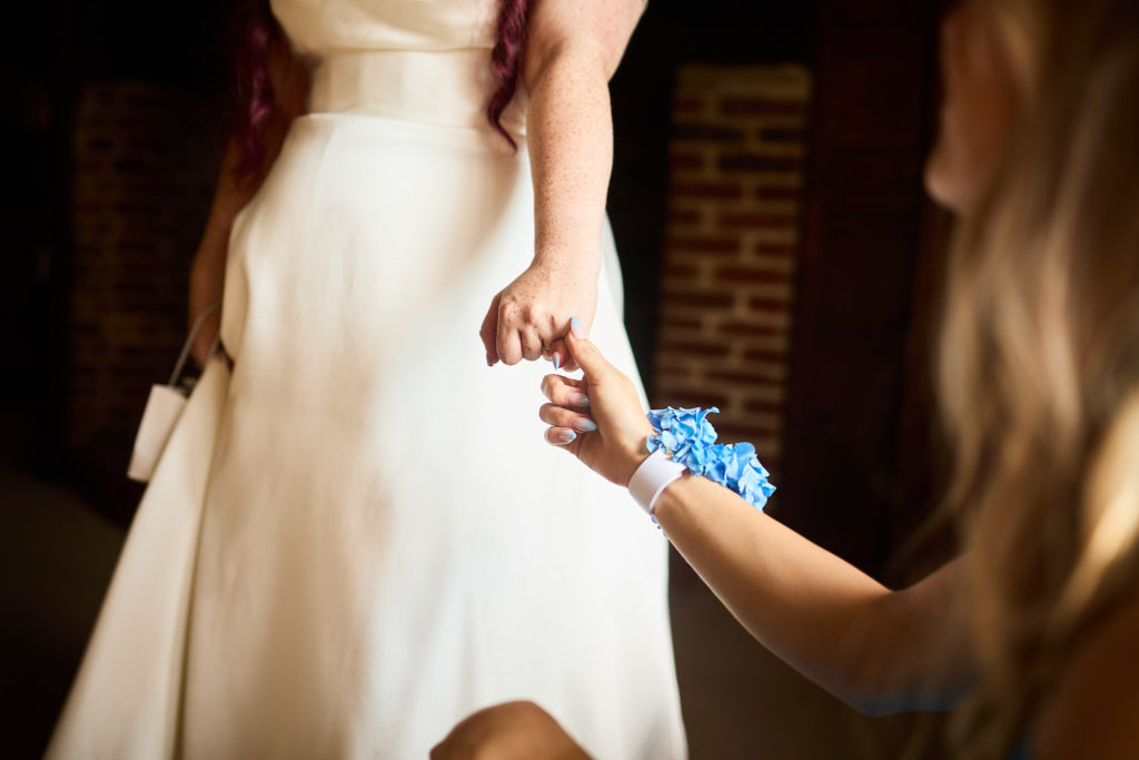 Close-up of the bride holding hands with a bridesmaid wearing a blue wrist corsage
