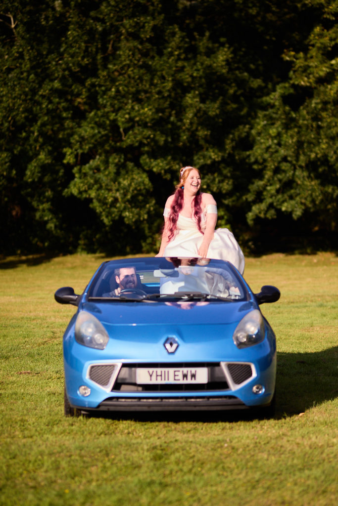 Bride sitting on the back of a blue Renault convertible on the lawn