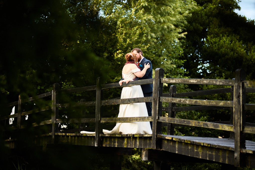 Bride and groom kissing on a rustic wooden bridge at Prested Hall in evening light