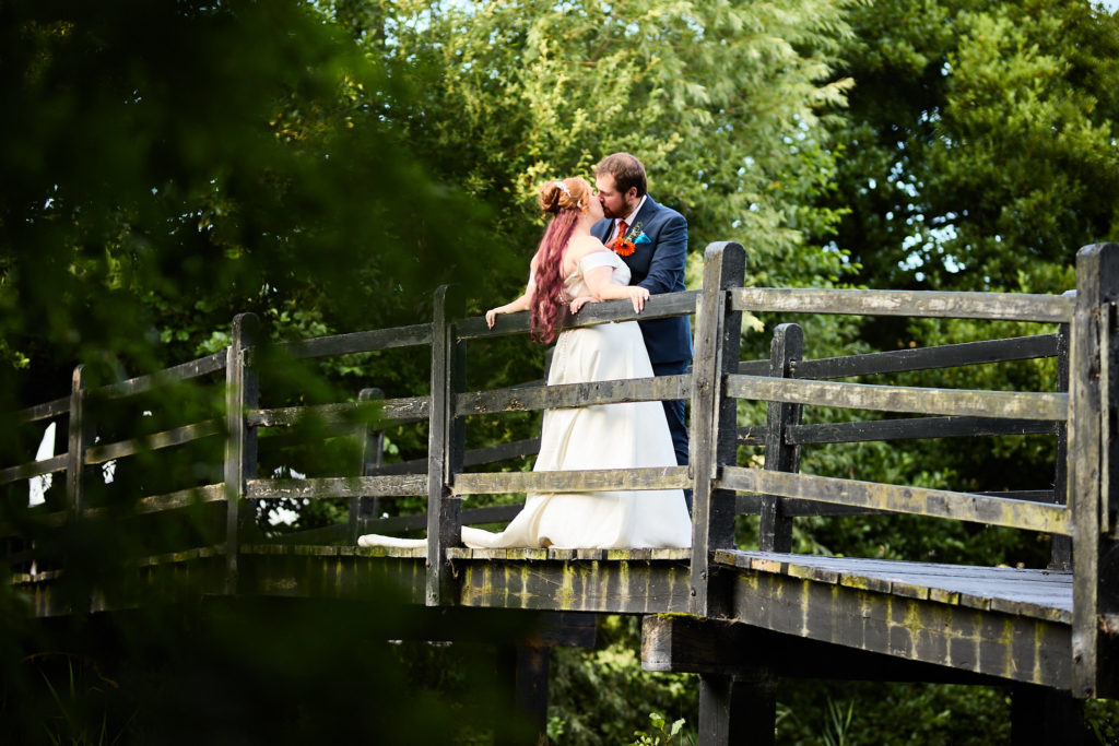 Bride and groom kissing on a wooden bridge surrounded by trees at Prested Hall, Essex