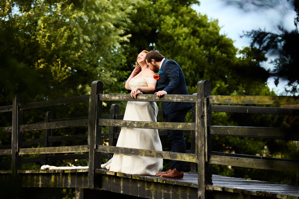 Bride and groom embracing on a wooden bridge in the grounds of Prested Hall, Colchester