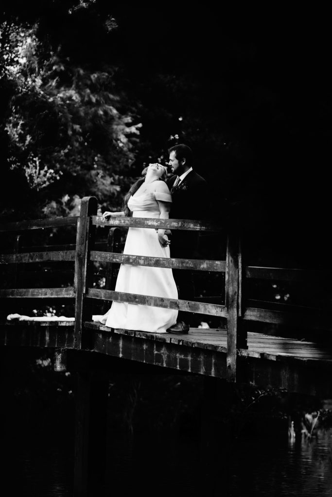 Black and white photo of the bride and groom kissing on a wooden bridge at Prested Hall