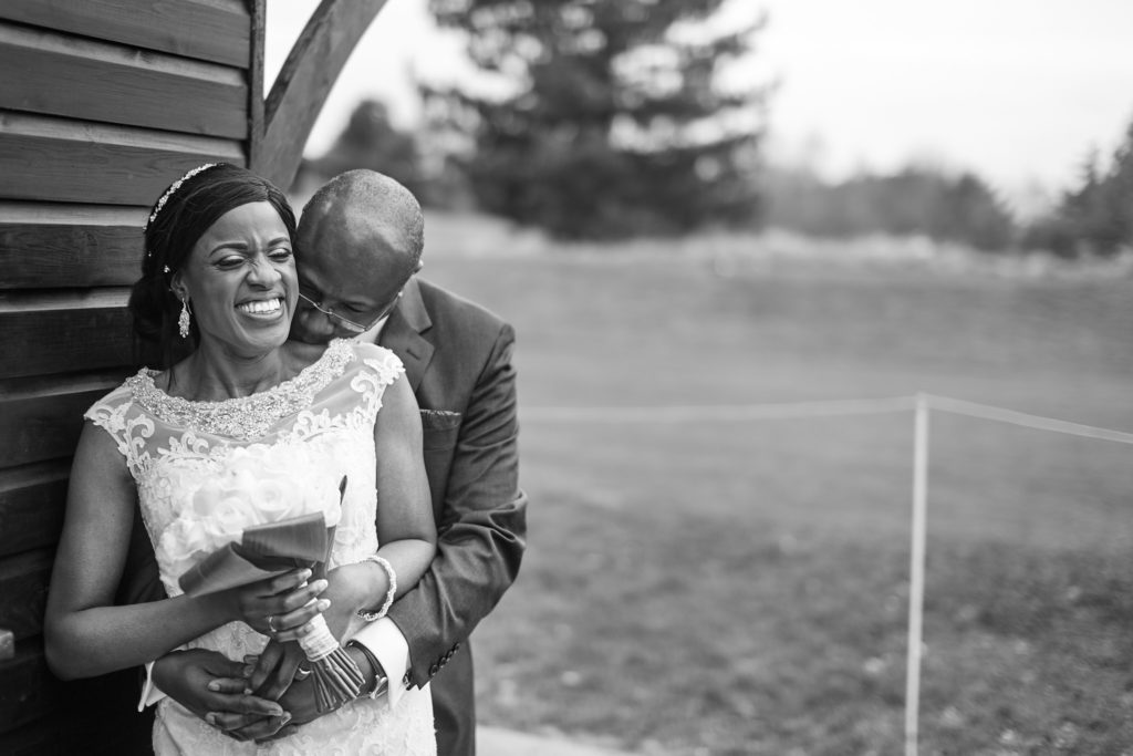 Black and white photo of the groom hugging the bride from behind at Essex Golf Club