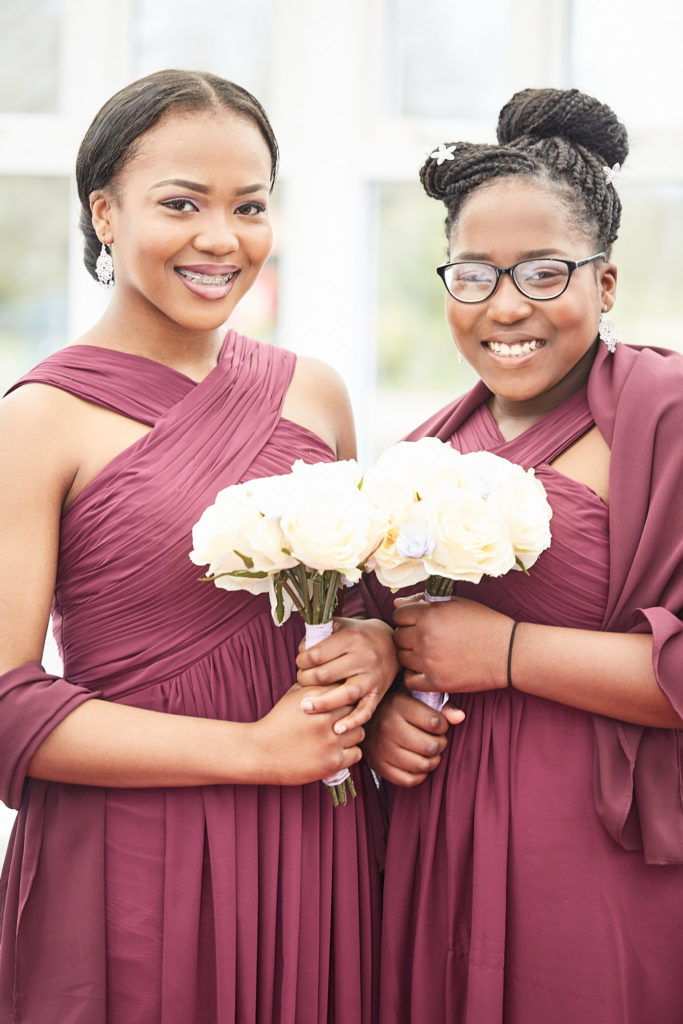 Two bridesmaids in burgundy dresses smiling with bouquets of cream roses