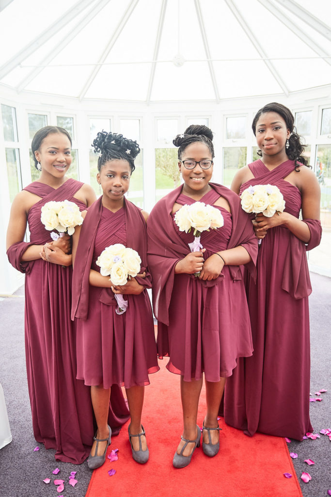 Four bridesmaids in burgundy dresses with cream bouquets on the red-carpeted aisle