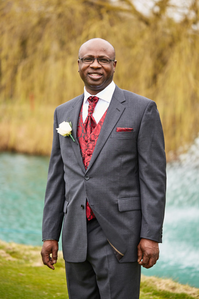 Groom in a grey morning suit and red waistcoat beside the lake and fountain at Essex Golf Club