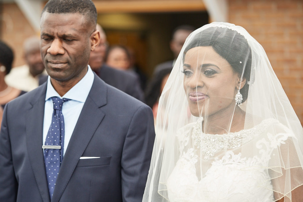 Bride in her veil arriving for the ceremony beside a man in a navy suit