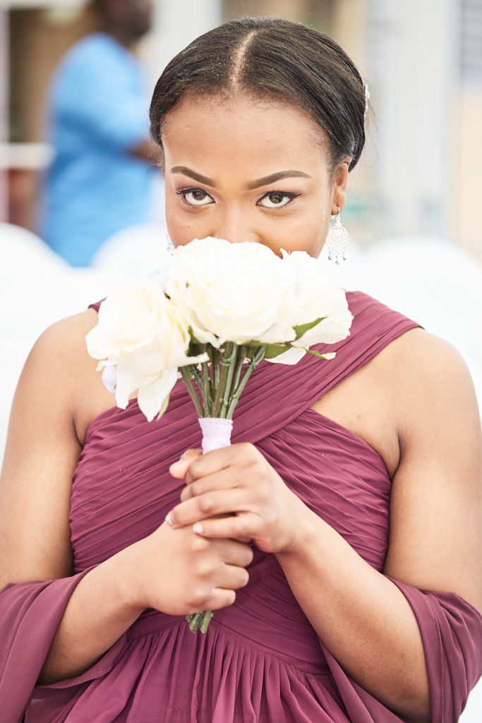 Bridesmaid in a burgundy dress peeking over her bouquet of cream roses