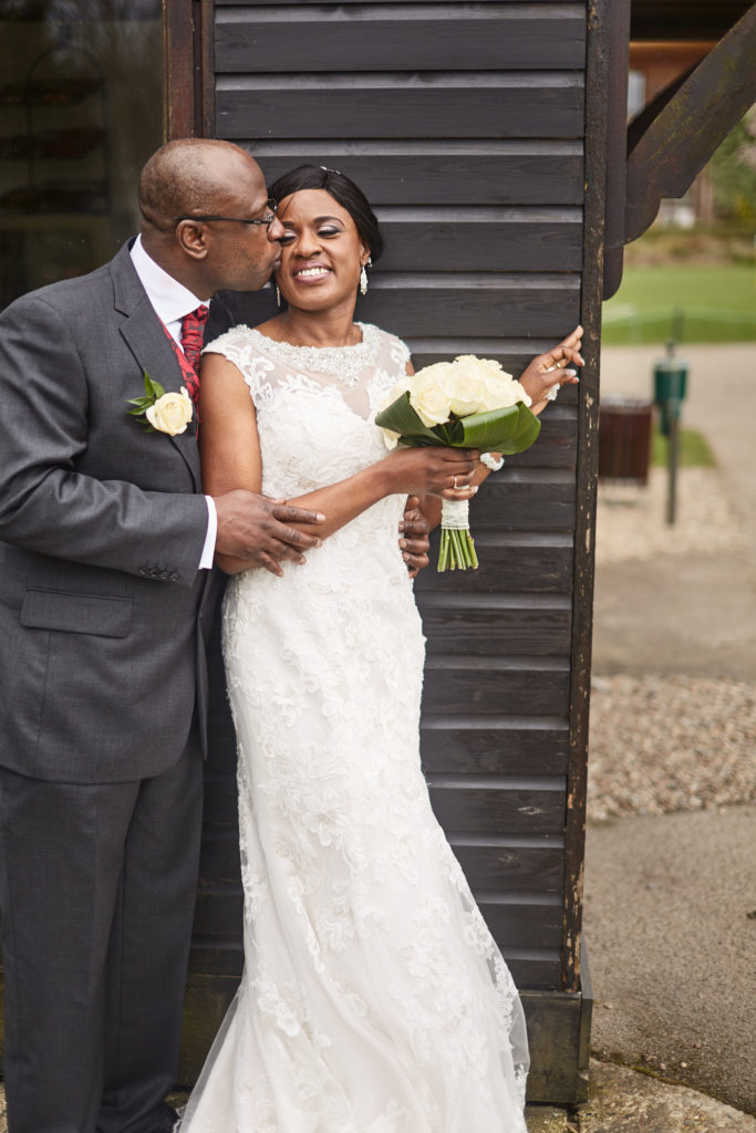 Groom kissing the bride's cheek as she laughs with her bouquet at Essex Golf Club