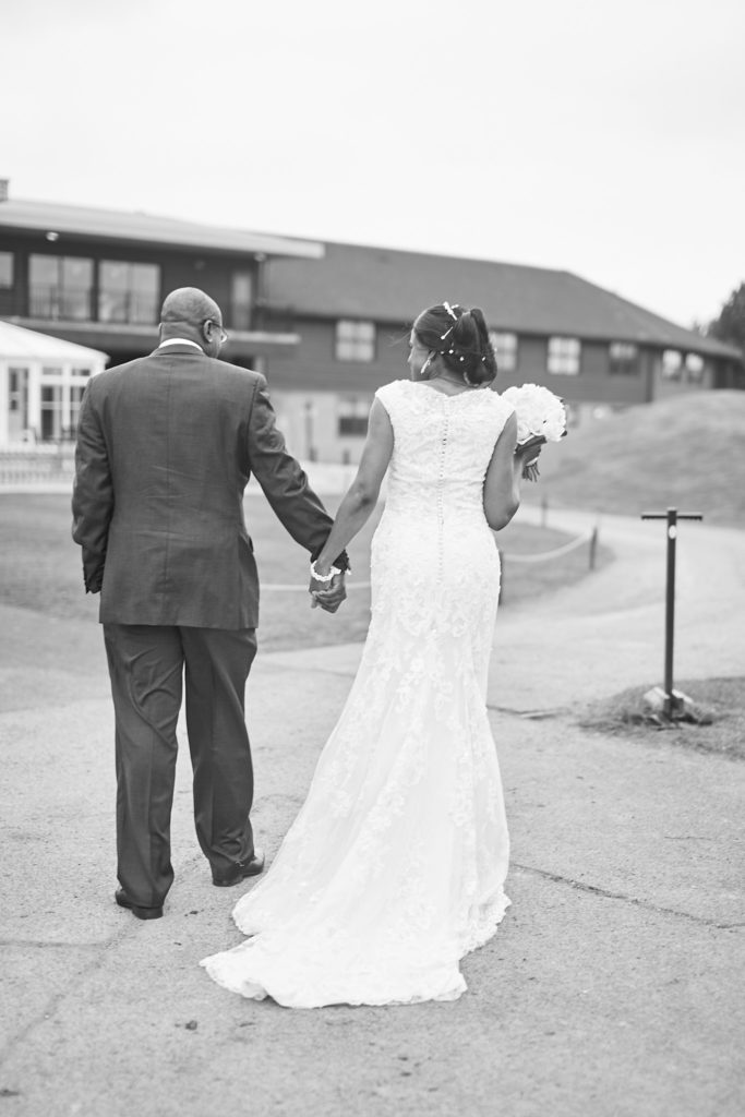 Black and white photo of the bride and groom walking hand in hand at Essex Golf Club, seen from behind