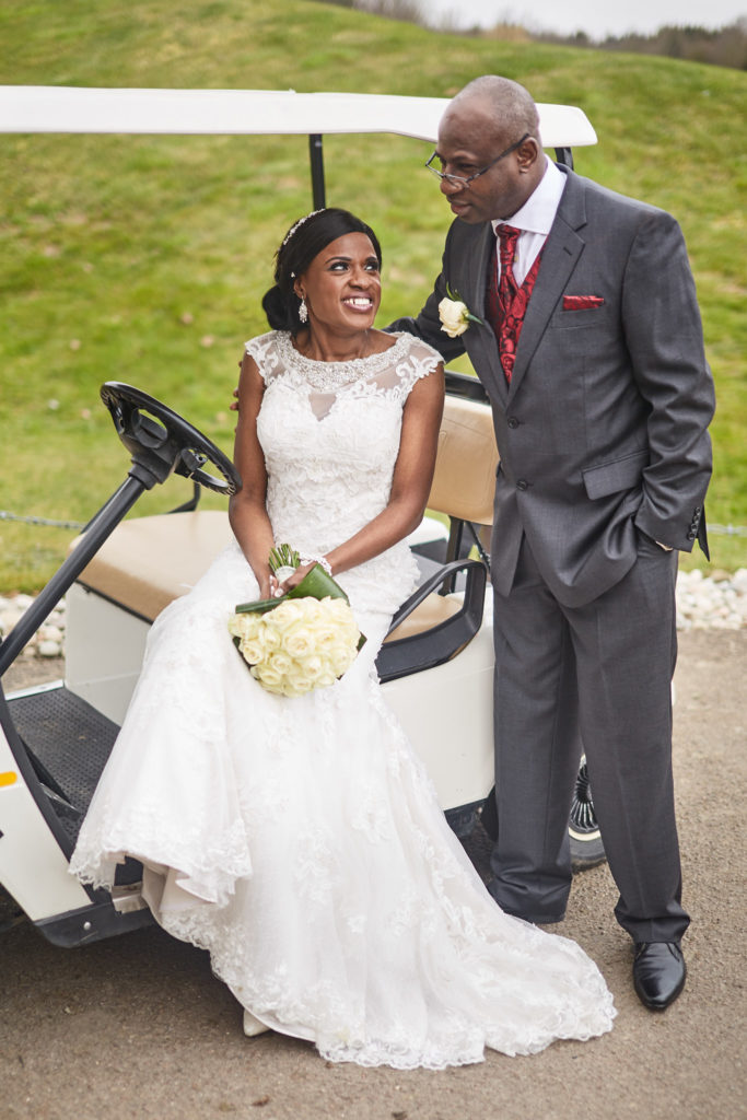 Bride sitting on a golf buggy with the groom standing beside her at Essex Golf Club