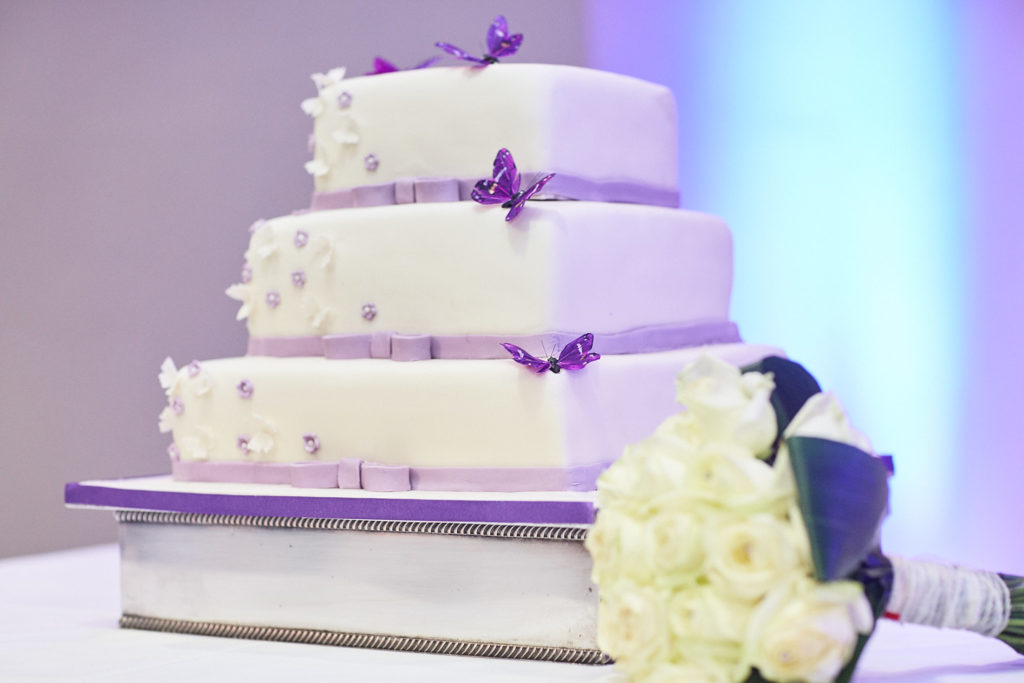 Three-tier white wedding cake with purple ribbon and cream roses