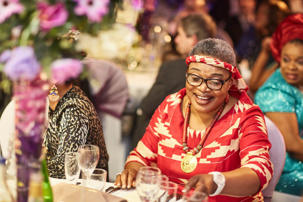 Guest in a red outfit and head tie smiling at the table